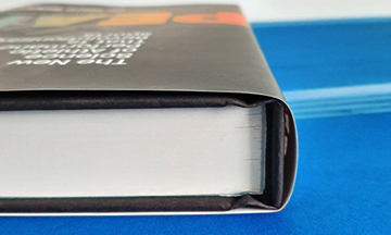 Profile view of a standard adhesive-bound hardcover book, highlighting the clean, square spine where the book block is glued to the outer case.
