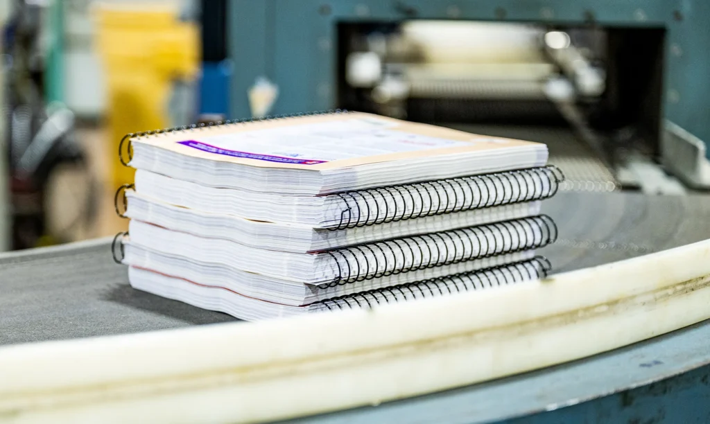 Close-up of a large-scale binding machine processing thick, durable commercial catalogs for manufacturers and distributors.