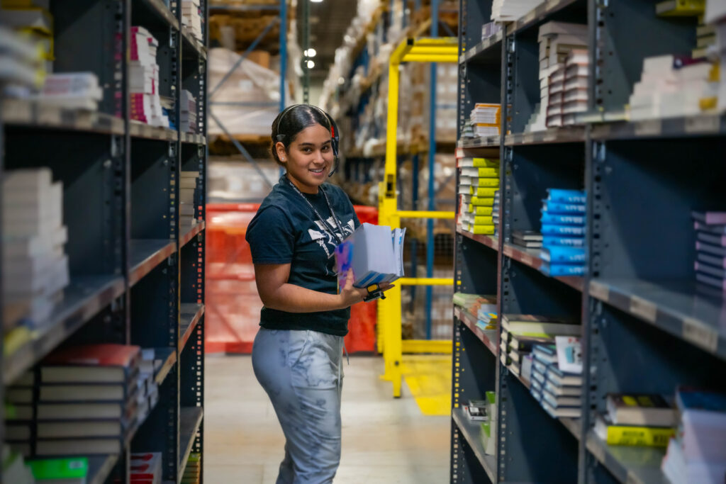 Lakeside Book employee smiling while picking book orders from a high-density warehouse shelf.